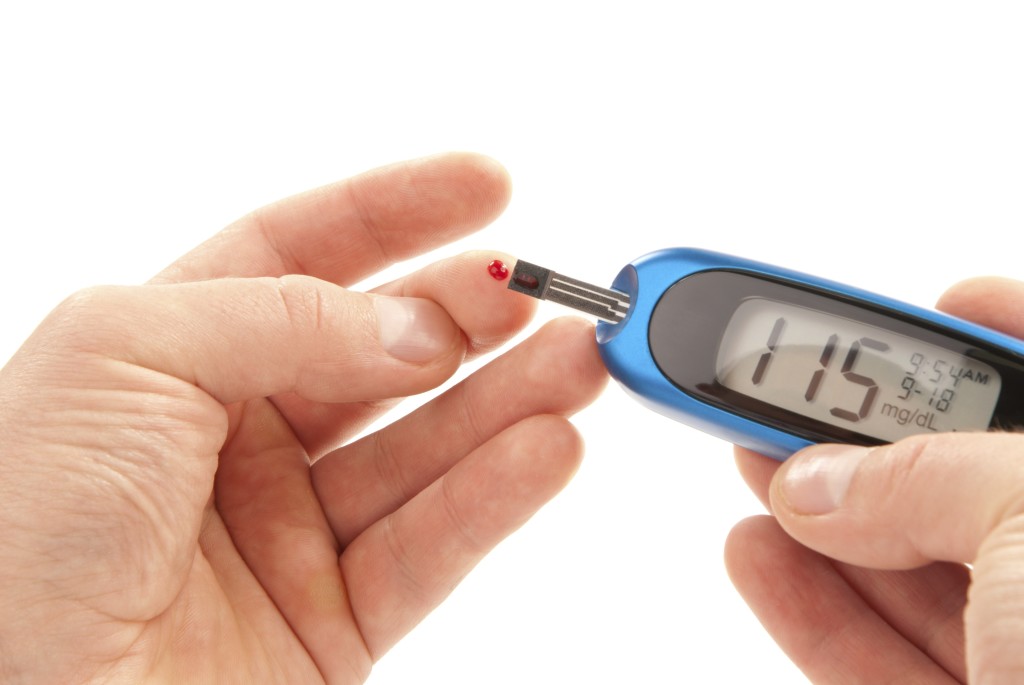 Diabetic patient doing glucose level blood test using ultra mini glucometer and small drop of blood from finger and test strips isolated on a white background. Device shows 115  mg/dL which is normal